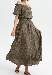 Maxiklänning med off-shoulder-design, brun tyg med ett svart abstrakt mönster, cinchad midja och en flödande kjol. Bruna sandals med kedjedetalj.