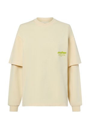 Crème-kleurig oversized T-shirt met een ronde hals en verlaagde schouders. Bevat groene bedrukte tekst op de borst. Van katoen.
