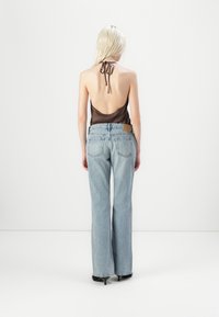 Top halter de satén marrón con espalda descubierta, combinado con jeans de mezclilla acampanados en un azul claro que cuentan con cinco bolsillos y un parche en la cintura trasera.