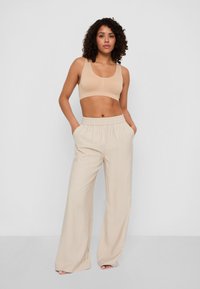 Pantaloni a gamba larga beige a coste con vita elastica, abbinati a un bralette aderente beige. Tessuto liscio e vestibilità rilassata.