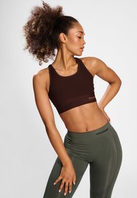 Bruine sportieve crop top gecombineerd met olijfgroene high-waisted leggings. De leggings hebben een geribbelde textuur en het merkembleem op de tailleband.