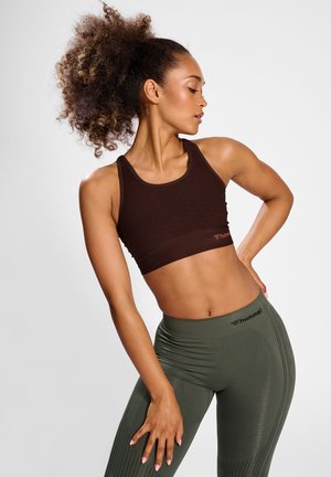 Bruine sportieve crop top gecombineerd met olijfgroene high-waisted leggings. De leggings hebben een geribbelde textuur en het merkembleem op de tailleband.