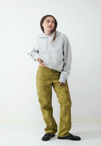 Szara bluza z kapturem z dużą kieszenią z przodu, zestawiona z spodniami w kolorze oliwkowym o wysokim stanie. Czarne buty typu slip-on dopełniają strój. Proste tło.