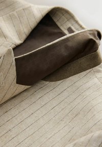 Blazer beige à fines rayures, col relevé, montrant la doublure intérieure marron foncé avec un motif à carreaux subtil.