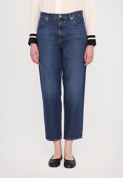 Dark blue denim jeans with a straight-leg design, featuring a high waist, five pockets, and a cuffed hem. Worn with black flats.