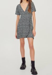 Vestido envolvente floral en blanco y negro con un escote en V profundo, mangas cortas y una tela texturizada. Combinado con botas de combate negras.
