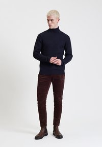 Maglione a collo alto in maglia navy abbinato a pantaloni in velluto a coste bordeaux e stivali alla caviglia in pelle nera. Silhouette semplice e aderente.