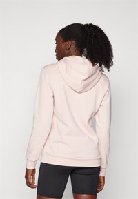 Sweatshirt rosa claro com capuz ajustável, punhos e bainha canelados. Usado com calções pretos, mostrando uma textura suave de algodão.