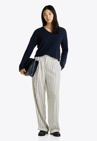 Granatowy sweter z prążkowanej dzianiny, spodnie w poziome paski o wysokim stanie z pionowymi wzorami oraz czarna torebka. Model ma na sobie czarne mokasyny.