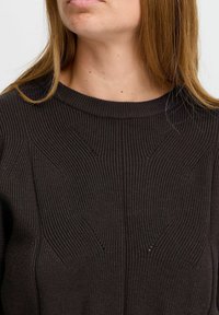 Mörk ribbad tröja med rund halsringning och texturerade mönster fram. Tyget verkar mjukt och något elastiskt.