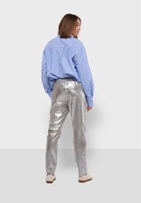 Zilveren metallic broek met een gladde textuur en een elastische tailleband, gecombineerd met een lichtblauw gestreept overhemd met knopen.