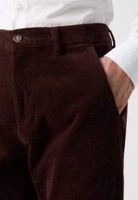 Bruna kordtöjbyxor med ribbad textur, knappstängning, sidofickor och en skräddarsydd passform. Matchas med en vit skjorta.