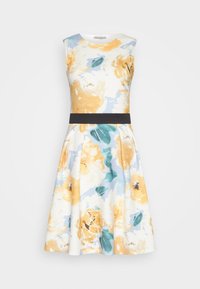 Vestido floral con patrones amarillos y verde azulado sobre un fondo blanco. Diseño sin mangas, corsé ajustado, cinturilla negra ceñida, falda acampanada.