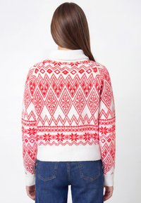 Suéter de patrón rojo y blanco con diseño geométrico, cuello y puños acanalados, y largo cropped. Textura suave de punto.