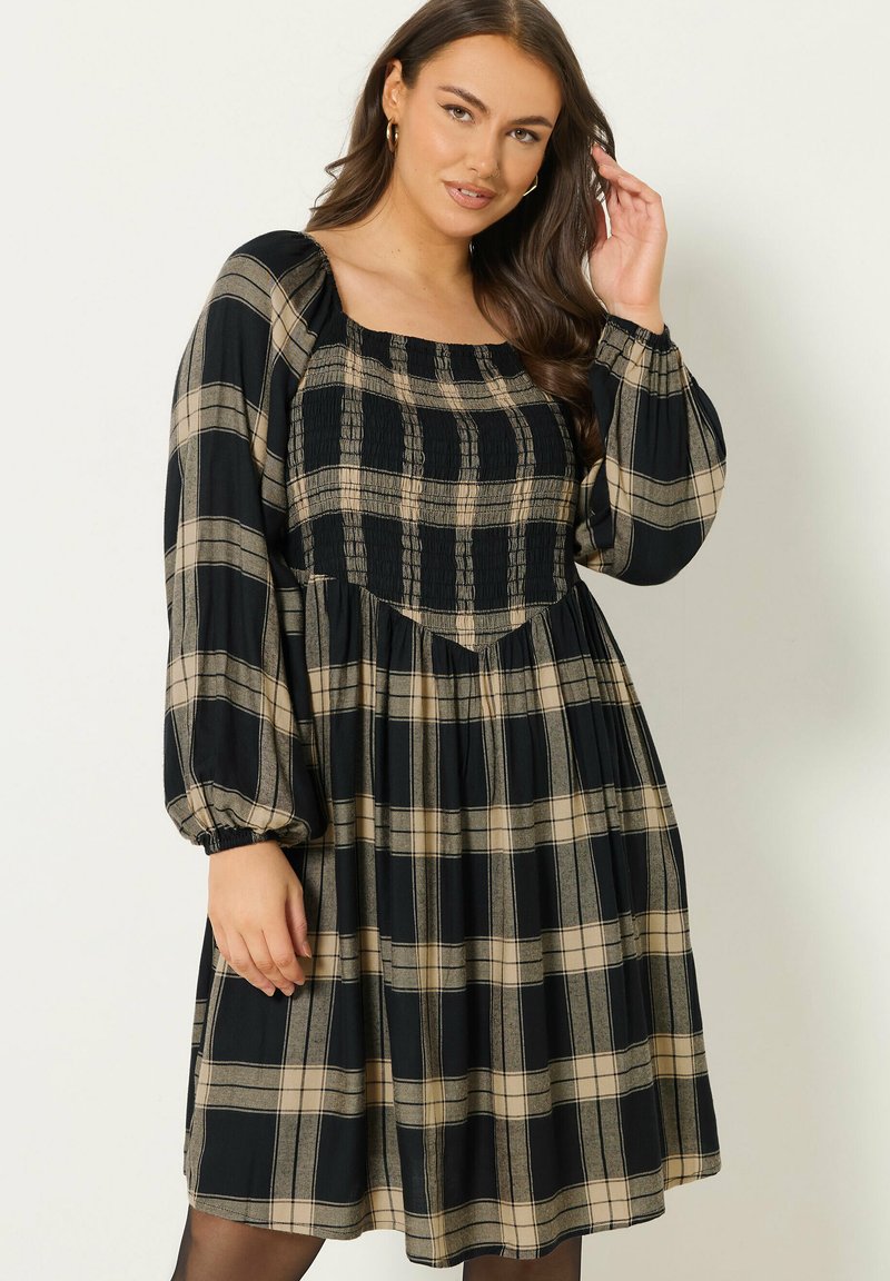 Vestido a cuadros en negro y beige con escote cuadrado, cuerpo fruncido y mangas abullonadas; hecho de tela ligera.