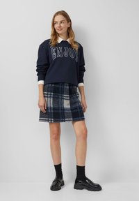 Sudadera navy con estampado de "ENJOY", combinada con una falda de franela de cuadros en navy, blanco y gris. Medias negras y mocasines brillantes completan el atuendo.