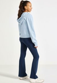 Jasnoniebieska, skrócona bluza z kapturem, o teksturowanym splocie. W połączeniu z ciemnoniebieskimi spodniami dzwonami. Uzupełnieniem stylizacji są białe snekaery.