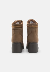 Bottes de cheville marron avec une tige texturée, des bouts ronds et un large talon noir. Présente un accent décoratif en fermeture éclair dorée.