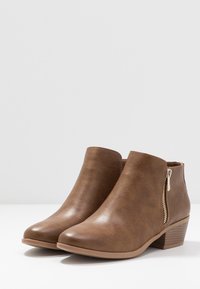 Bottes courtes en similicuir marron à finition texturée, avec une fermeture éclair latérale, un bout amande et un petit talon empilé pour plus de stabilité.