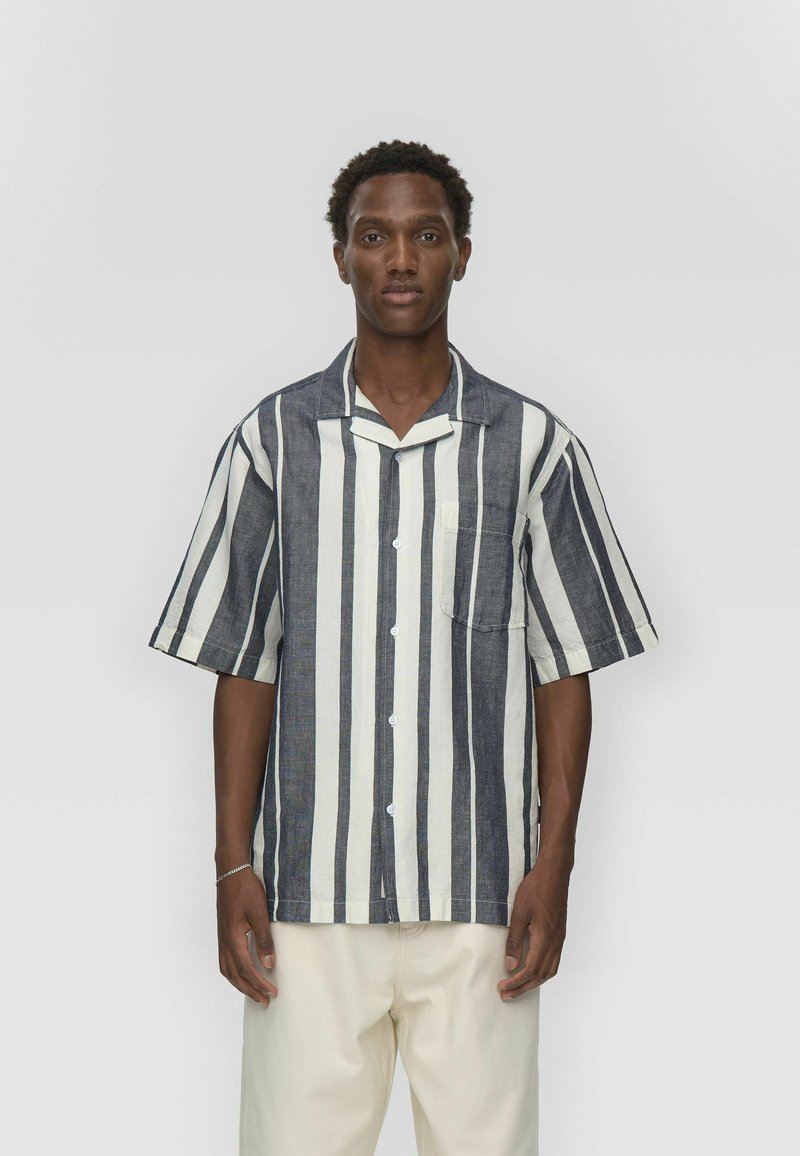 Chemise à manches courtes rayée en bleu marine et blanc ; comprend une fermeture à boutons sur le devant et une poche poitrine ; fabriquée en tissu léger.