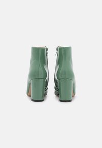 Botines de charol verde con tacón grueso, cierre de cremallera en la parte trasera y acabado suave y brillante.