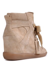 Baskets compensées en daim beige avec semelle en gomme, épaisses lacets tressés, clous en métal au talon, et une étiquette en daim portant la mention « BRONX » fixée aux lacets.