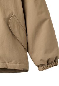 Kurtka w kolorze brązowym o miękkiej fakturze, z elastycznymi mankietami i boczną kieszenią z zakrzywioną klapką. Gładki, lekko luźny krój.