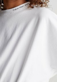 T-shirt in cotone bianco con scollo a girocollo e logo "Calvin Klein Jeans" lungo il colletto. Tessuto morbido con vestibilità rilassata.