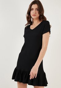 Black short-sleeve dress made from ribbed fabric, featuring a V-neckline and a ruffled hemline for added detail.
