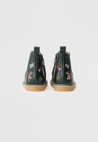 Botas de tobillo de cuero verde con bordados coloridos de animales y naturaleza, suela beige y cremallera lateral. Ribete cosido a lo largo de la suela.