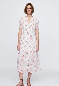 Kvetinové midi šaty z ľahkej látky, s krátkymi nadýchanými rukávmi, zapínaním na gombíky vpredu a opaskom v páse. Farby zahŕňajú bielu, červenú a modrú.