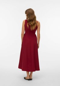 Burgundijas bezmugurkaula maksi kleita ar pielāgotu augšdaļu, izplūdušu apakšmalu un smalkām krokām. Valkāta ar minimālisma melnām sandaļām.