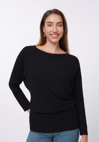 Juoda ribinė ilgarankovė palaidinė su plačia iškirpte, laisvo silueto ir tekstūruoto audinio. Derinama su mėlynais džinsais.