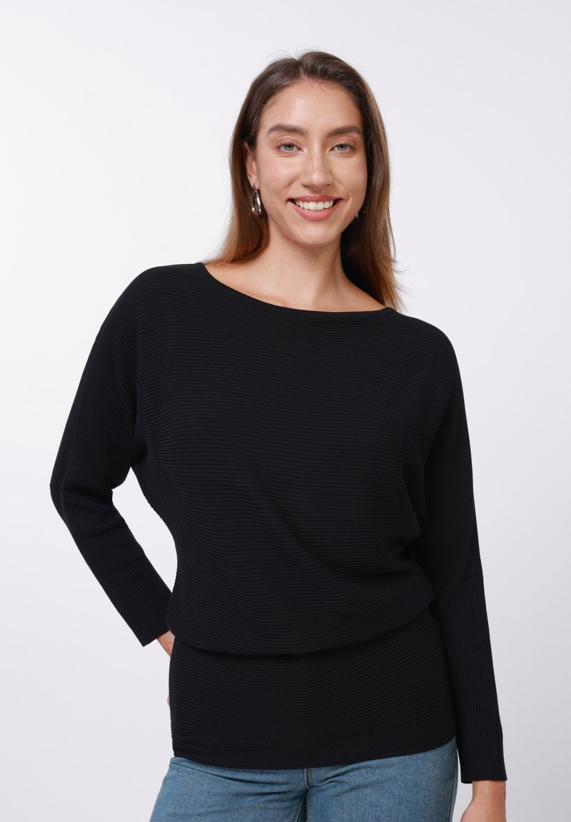Juoda ribinė ilgarankovė palaidinė su plačia iškirpte, laisvo silueto ir tekstūruoto audinio. Derinama su mėlynais džinsais.