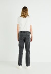Jeans de mezclilla gris con corte recto, detalles de costura visibles y un diseño clásico de bolsillo, combinados con una camiseta blanca sencilla.
