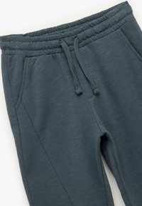 Mørkegrå joggebukser med elastisk talje, snor og sidelommer. Stof har en blød, struktureret overflade.