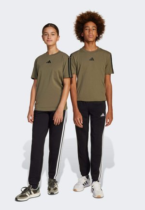 Olijfgroene t-shirts met zwart adidas-logo, gecombineerd met zwarte broeken met witte strepen aan de zijkanten, gedragen door twee staande modellen.