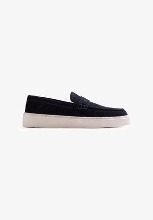 Mocassino slip-on in suede nero con suola spessa in gomma bianca e dettagli cuciti su sfondo bianco.