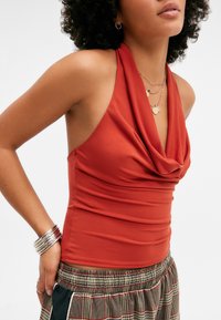 Top halter de color óxido con escote drapeado, hecho de una tela suave. Presenta un diseño ajustado y se combina con pantalones sueltos de estampado.