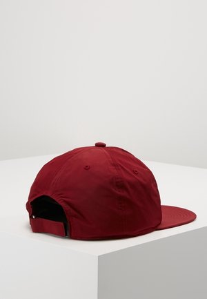 Casquette de baseball rouge ajustable posée sur une surface blanche, vue de dos avec une sangle fermée et des panneaux cousus.
