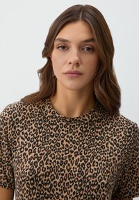 Leopardenmuster Kurzarmtop mit Rundhalsausschnitt. Weicher, strukturierter Stoff in Brauntönen und Schwarz mit lockerer Passform.