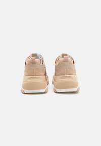 Scarpe sportive beige con una morbida tomaia in suede, suole bianche, linguette di trazione e dettagli testurizzati sul tallone e sulla linguetta. Nome del marchio sul tallone.