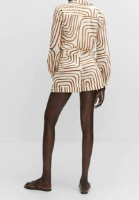 Camicia a maniche lunghe beige e bianca a fantasia, con vita a cintura, abbinata a pantaloni corti coordinati. Tessuto liscio con una vestibilità ampia.