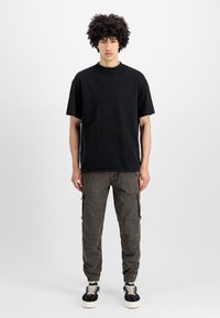 T-shirt preta de algodão com mangas curtas, combinada com calças cargo em verde-oliva com vários bolsos e bainhas ajustadas.
