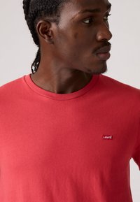 T-shirt rouge à col rond en coton avec une texture lisse, arborant un petit logo rouge Levi's sur la poitrine.