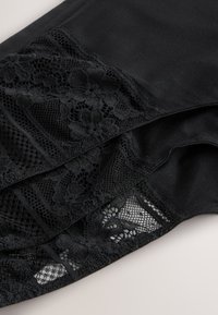 Sorte leggings med blonder detaljer i blomsterdesign og mesh teksturer. Stoffet er elastisk med en glat overflade.