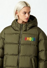 Doudoune vert olive avec capuche, ornée d'une broderie "AMOUR" multicolore. Texture matelassée et fermeture éclair pour la chaleur.