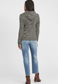 Grå stickad huvtröja med ett strukturerat mönster, med en rymlig huva. I kombination med ljusblå raka jeans och bruna ankelskor.