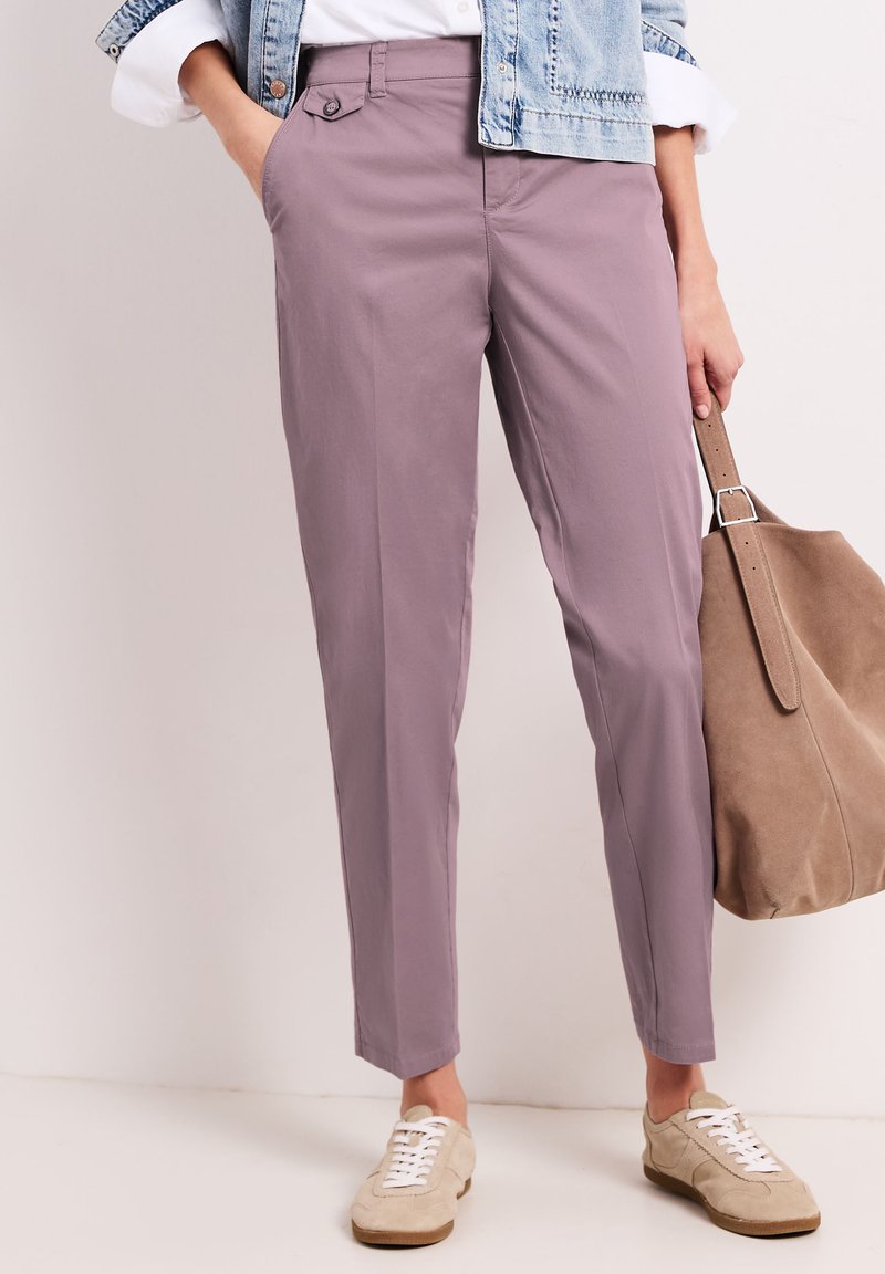 Mujer con pantalones estrechos color malva, zapatillas beige, chaqueta vaquera y un gran bolso tote de ante color tostado a su lado.