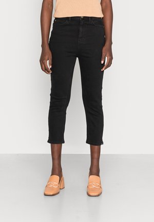 Zwarte cropped jeans met een aansluitend ontwerp, vijf-pocketstijl en een ritsdetail aan de zoom, gecombineerd met tan hoge instapschoenen.